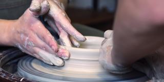 陶工师傅和他的学生用手在陶工转盘上磨平杯子的边缘