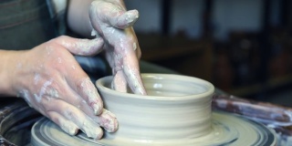 陶工学徒的双手正试图在陶工轮上对齐产品的边缘
