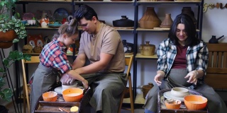 一个年轻的家庭和一个学龄前的女儿在陶器大师班做陶制杯子