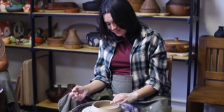 一位年轻女子微笑着在陶工转盘上磨平一只粘土杯的边缘