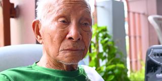 一个九十多岁的亚洲人坐在家里，在他的辛苦工作中放松他的一生。