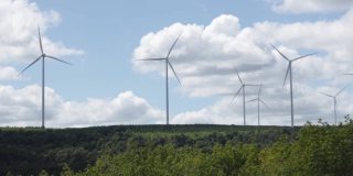 大型风力涡轮机旋转叶片在山上的背景森林，蓝天和云。替代能源。