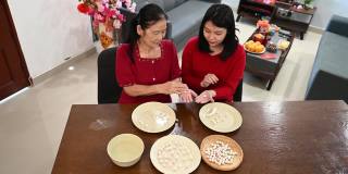 一位亚洲的奶奶和她的孙女正在为庆祝中国新年而准备汤圆