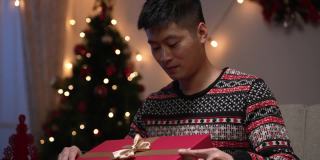 一名中国男子惊讶地捂着嘴，用“是”的手势庆祝，对自己在节日的家中得到的圣诞预设感到满意