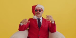 穿着红色西装、戴着圣诞老人帽、戴着红色滑稽眼镜的小胡子男子坐在椅子上，突然收到一份惊喜礼物，感到很开心。新年销售和促销惊喜哇概念
