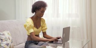 一名非裔美国女性自由职业者，在家工作。女人在笔记本电脑前开心的笑着。彩票中奖，雇佣，股票上涨，加密货币增长，好消息。举起手来