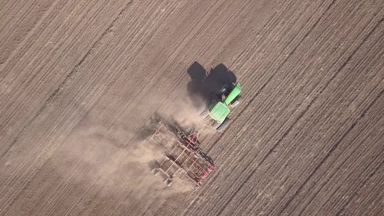 绿色拖拉机从上到下鸟瞰图的耕地和播种干燥的田野。农民在早春季节用苗床耕田作为播种前活动的一部分