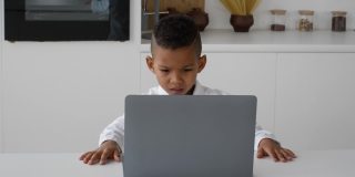 黑人男孩在家用笔记本电脑学习，皱着眉头看着屏幕