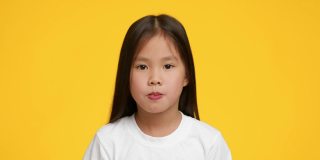 一个韩国小女孩在黄色背景上嚼和吹泡泡糖