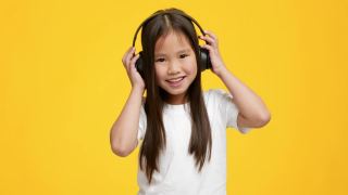 小亚洲女孩听音乐戴耳机，黄色背景视频素材模板下载