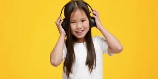 小亚洲女孩听音乐戴耳机，黄色背景