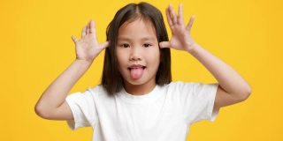 搞笑的韩国小女孩伸出舌头做鬼脸，黄色背景