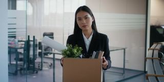 被解雇的亚洲妇女扛着箱子离开室内解雇后的工作场所
