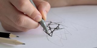 在一张纸上的特写画，手拿着记号笔线，勾勒出用灰色铅笔画的草图。设计师或艺术家的作品神经学和心理治疗
