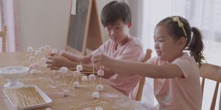 混合种族的亚洲儿童用意大利面和棉花糖建造塔，在家远程学习，STEM科学，在家教育，社交距离，蒙特梭利概念