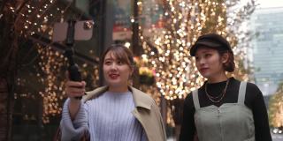 年轻的女性朋友们在圣诞节的灯光下在城市里拍视频