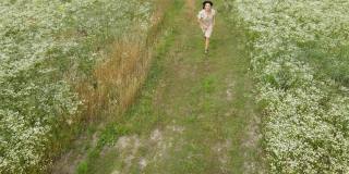 无人机鸟瞰图快乐女人穿着在鲜花盛开的草地，在乡下，在夏天的一天，在田野里，感受大自然，放松，独自旅行。缓慢的运动。