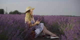 在薰衣草地里，戴着帽子的金发女郎坐在灌木丛中，制作薰衣草花束，微笑着欣赏夏日的日出或日落。自然与旅游理念。