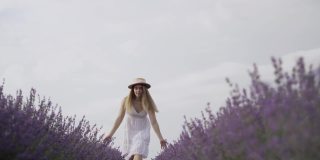 年轻美丽的白人妇女在夏天的黎明戴着草帽沿着薰衣草田底部的观点。