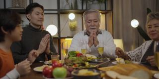 亚洲大家庭在家里吃饭前祷告祷告，祷告时闭上眼睛和双手