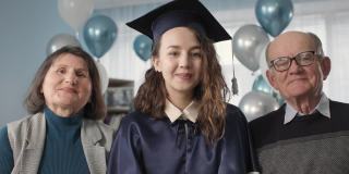 快乐的女毕业生的肖像，在学术帽和长袍与快乐的父母庆祝在线毕业在线连接的方式，看相机