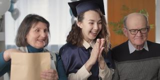 在远程教育、隔离期间，身着学士帽、学士服的快乐女孩与快乐的父母一起在线庆祝毕业和毕业