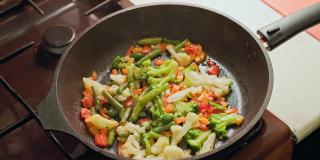 白种人的手搅拌蔬菜在煎锅与不锈钢叉子，而油炸，特写