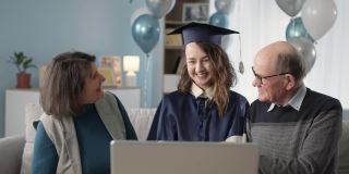 在线毕业典礼，可爱的父母和女儿在家客厅通过视频庆祝毕业