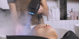 洗完头发后，一名女子躺在美发师面前，用手持式蒸笼将头发吹干。