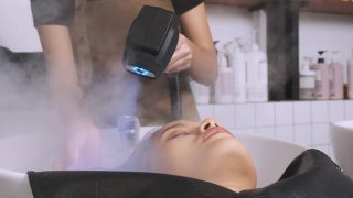 洗完头发后，一名女子躺在美发师面前，用手持式蒸笼将头发吹干。视频素材模板下载