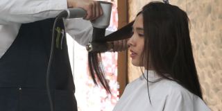 在现代美容院，美发师用吹风机给美女做头发。