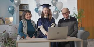 高中毕业，高兴的父母祝贺女毕业生毕业，并在一个在线典礼上给她颁发毕业证书坐在家里的客厅里，气球在