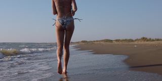 日落时分，穿着比基尼的女孩在海滩上奔跑，溅起水来。以120fps记录的慢动作