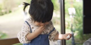 一个调皮的日本小女孩拿着叉子站在椅子上玩午餐时间，正在往嘴里吐面包。