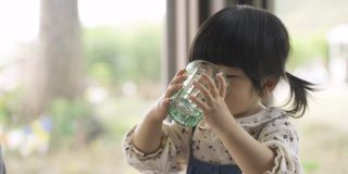 一个口渴顽皮的亚洲小女孩在模糊的玻璃窗户背景下从杯子里流口水和吐水的肖像。