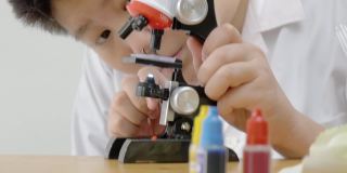亚洲男孩穿着实验服，在学校实验室使用显微镜进行测试，教育的生活方式理念。