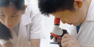亚洲儿童穿着实验服，用显微镜做科学实验，在家学校实验室，教育生活理念。