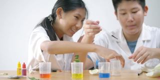 亚洲学校的孩子们穿着实验室的大褂在盛水的烧杯里撒颜色，科学实验，