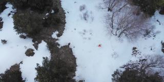 鸟瞰图，一名身穿橙色套装的滑雪者沿着春天森林里的残雪滑行。春季极速滑雪