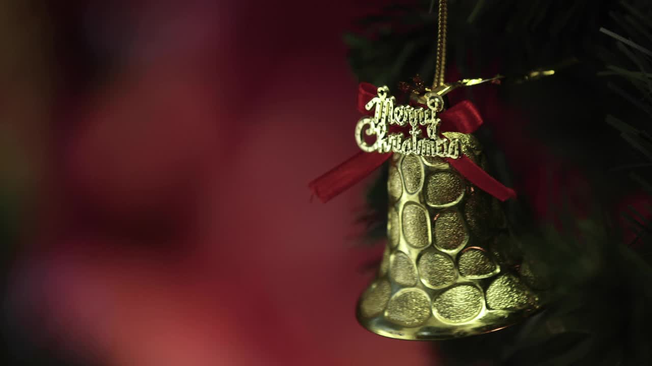 圣诞祝福的话语，金色的装饰铃铛挂在松树枝上，壁炉的火焰在模糊的背景中。圣诞装饰的想法和快乐的年底。