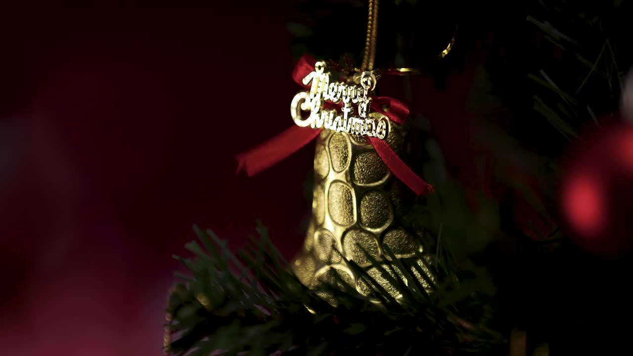 圣诞祝福的话语，金色的装饰铃铛挂在松树枝上，壁炉的火焰在模糊的背景中。圣诞装饰的想法和快乐的年底。