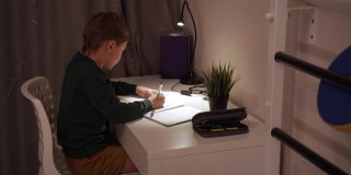 一个白人男孩在家里的灯光下做作业