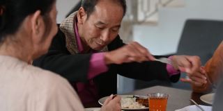 中国农历新年，一位亚洲老人在家中享用团圆饭时，与妻子分享食物