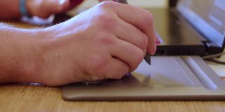 平面设计师的手在工作。他在笔记本电脑显示器前使用手写笔在一个图形平板电脑上
