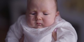 家中爆头，面部表情不满意。特写白人婴儿的灰色眼睛在女性的手。婴儿期和生活方式。