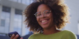 非裔美国妇女在镜头前微笑，手里拿着智能手机，科技