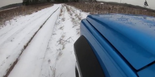 蓝色的汽车在雪地上行驶。从引擎盖上看。穿越森林道路的时间间隔。