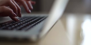 近距离侧面视图的手，不认识的商业妇女使用打字在笔记本电脑键盘上坐在家里的办公桌上工作在线。