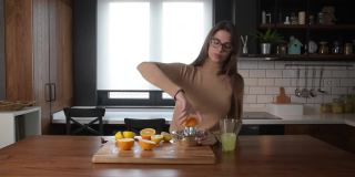年轻的商业妇女在去工作之前，在厨房用橙子水果和柠檬制作维生素炸弹能量饮料果汁。女性健康生活理念。