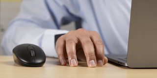 靠近一个白人男子的手，焦急地敲打她的桌子与他的手指，而工作在一个笔记本电脑在办公室。与工作相关的焦虑、压力、无聊、不耐烦和紧张的概念